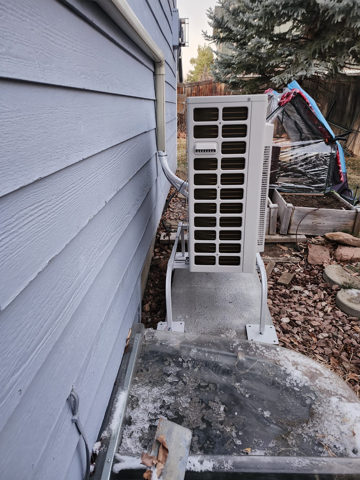 Mini-split condenser installed on raised stand for snow clearance and airflow.