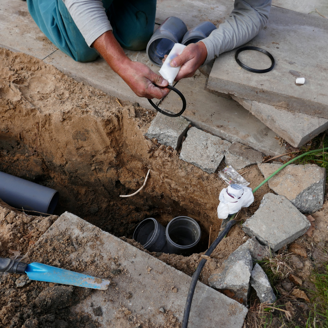 A plumber working outside on a sewer line with pipes and tools