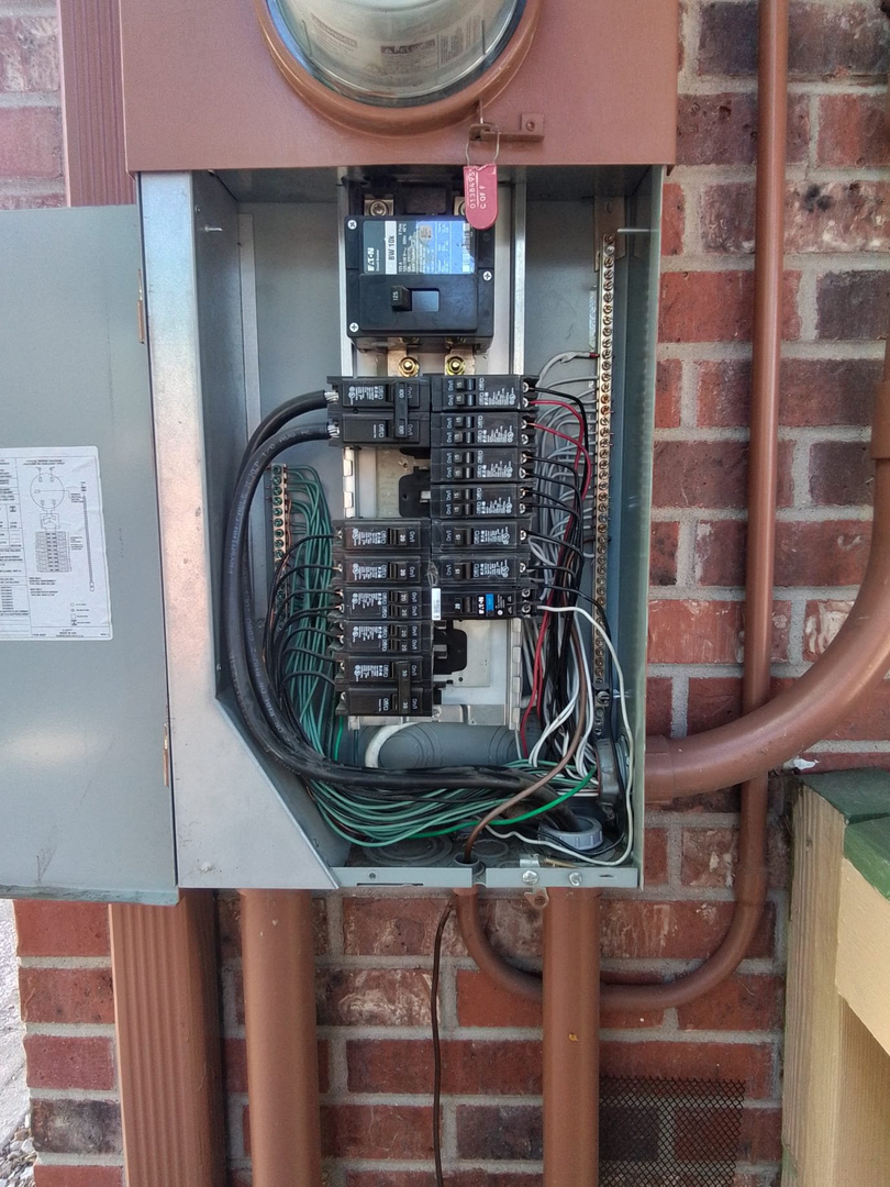 Open electrical panel mounted on a brick wall with wires