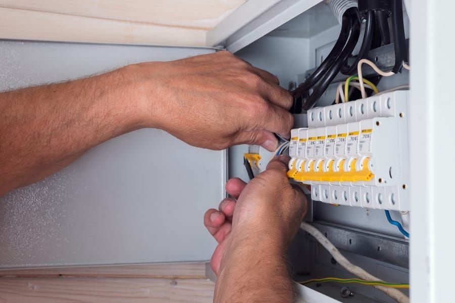 Close-up of hands wiring a breakers panel inside an electrical cabinet.